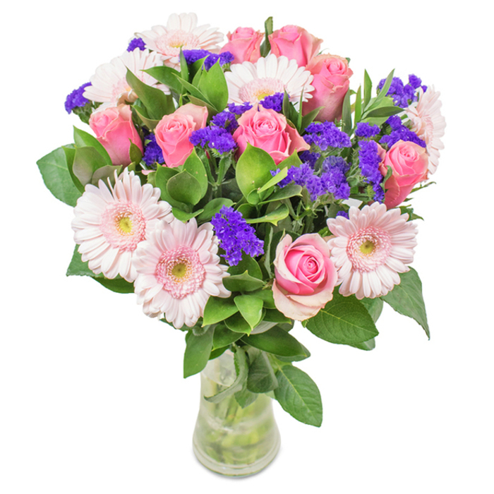 Set against a clean white background, this striking bouquet showcases around 7-9 pink roses-each flower marked by classic, tightly furled petals or gently opening into signature spirals. Alongside are approximately 5-7 pale pink Gerbera daisies with expansive heads and pale, almost white, centers, their cheerful presence unmistakable. Sprigs of vivid purple statice are nestled throughout, delivering visual texture and lively depth. A base of rich, deep green foliage imbues the bouquet with the freshness and vibrancy one might find outdoors in Limehouse's leafy parks or along the Regent's Canal. The transparent glass vase reveals the stems and water, highlighting the bouquet's natural origins and freshness so often seen at Flowers Limehouse. Perfect for the area's anniversaries, birthdays, or making spaces along Narrow Street feel more inviting, this arrangement blends harmonious pinks and purples, sending messages of joy, affection, and celebration deeply rooted in Limehouse's welcoming spirit.
